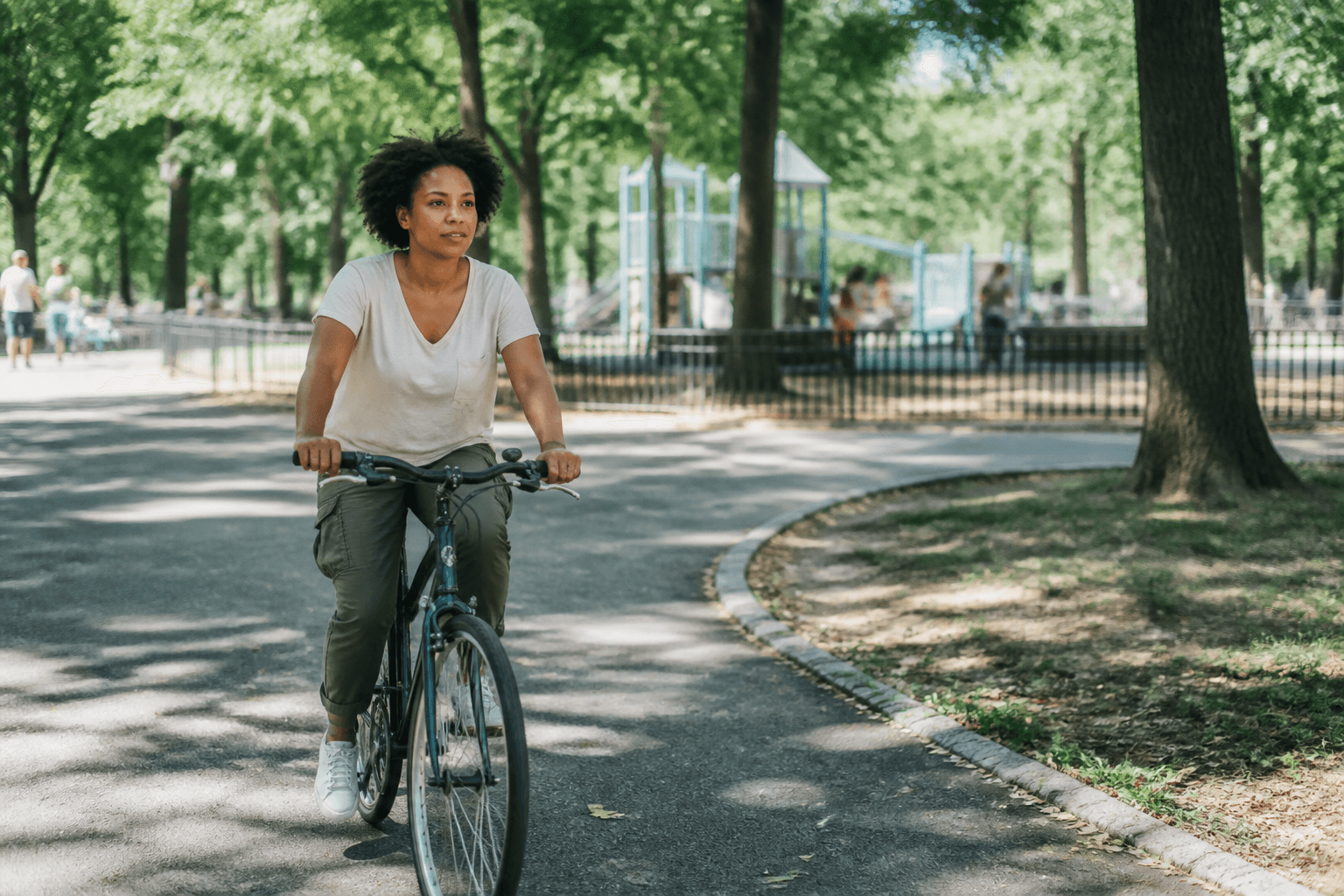 A parent riding a bicycle on a paved path through a neighborhood park